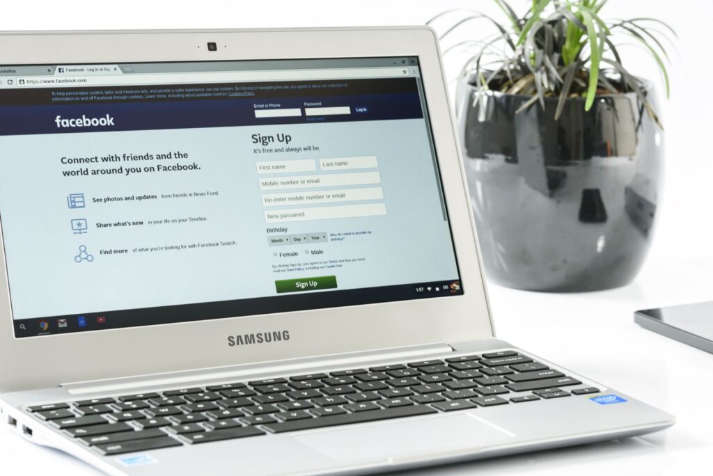 Samsung laptop displaying Facebook sign-up page beside a potted plant symbolizing DIY versus pro Facebook management