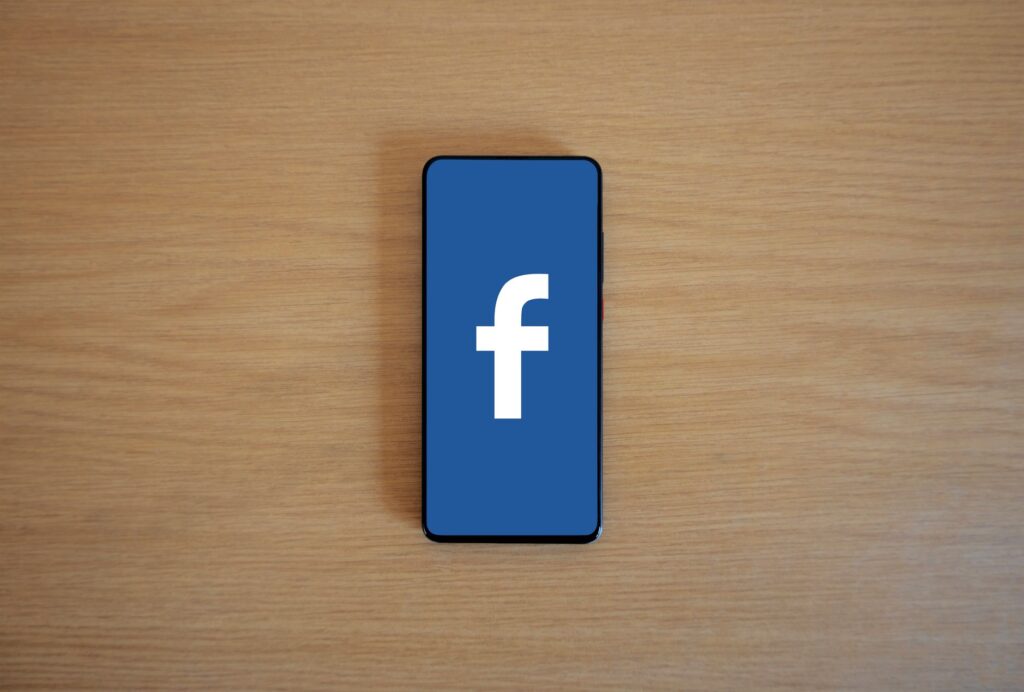Smartphone displaying Facebook logo on wooden surface for home services Facebook ads guide by Websza