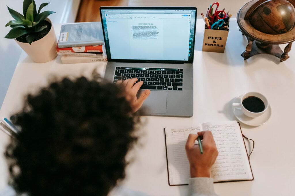 Anonymous writer working on blog writing at a laptop with a hot drink and diary on the table